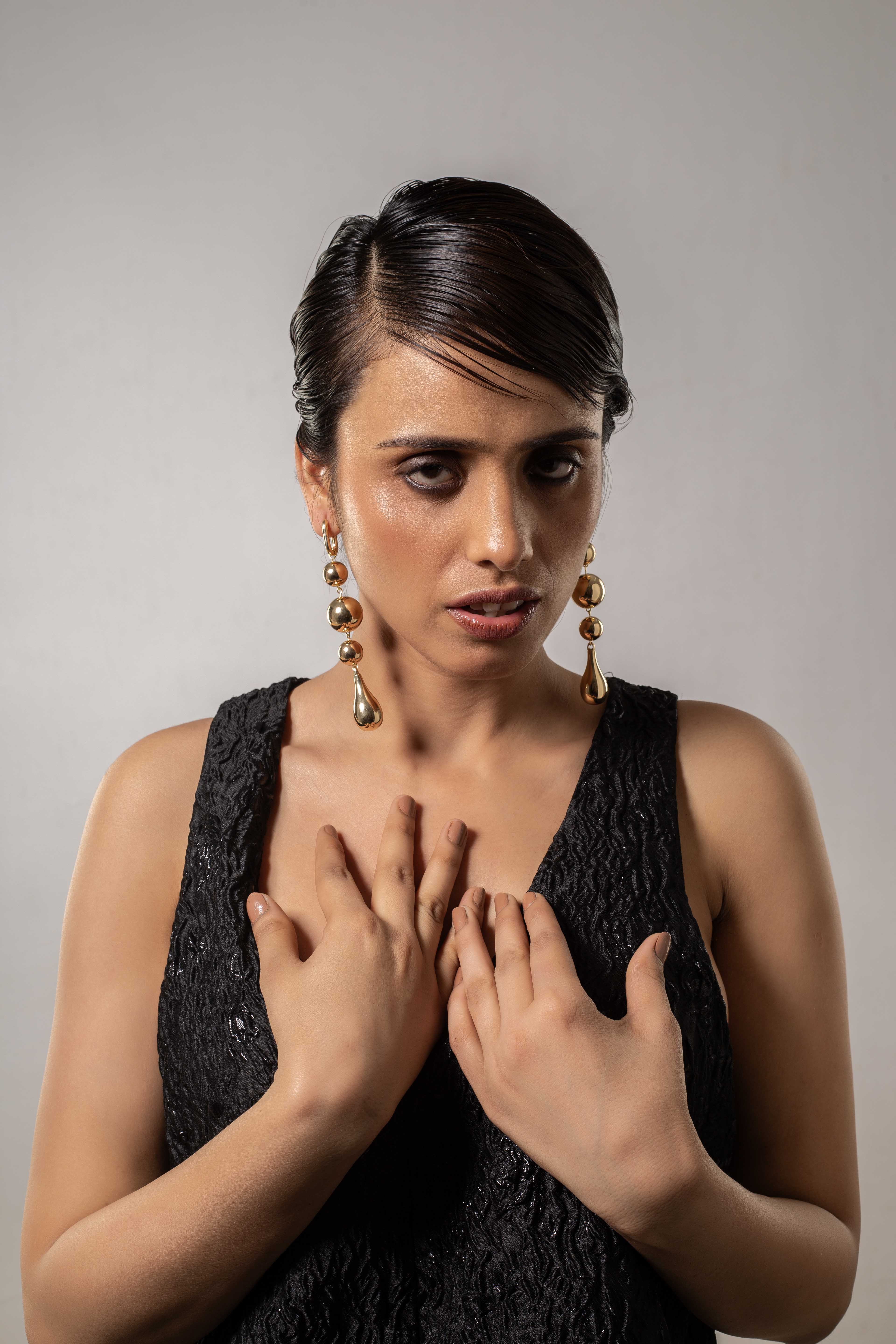 Woman wearing a black dress and gold earrings against a gray background