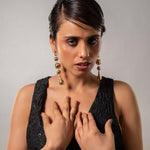 Woman wearing a black dress and gold earrings against a gray background