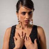 Woman wearing a black dress and gold earrings against a gray background